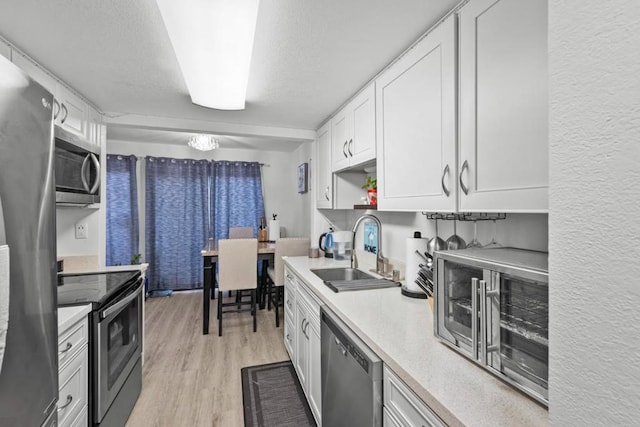 kitchen with a textured ceiling, appliances with stainless steel finishes, white cabinetry, sink, and light wood-type flooring