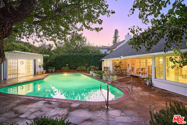 pool at dusk with an outbuilding and a patio area