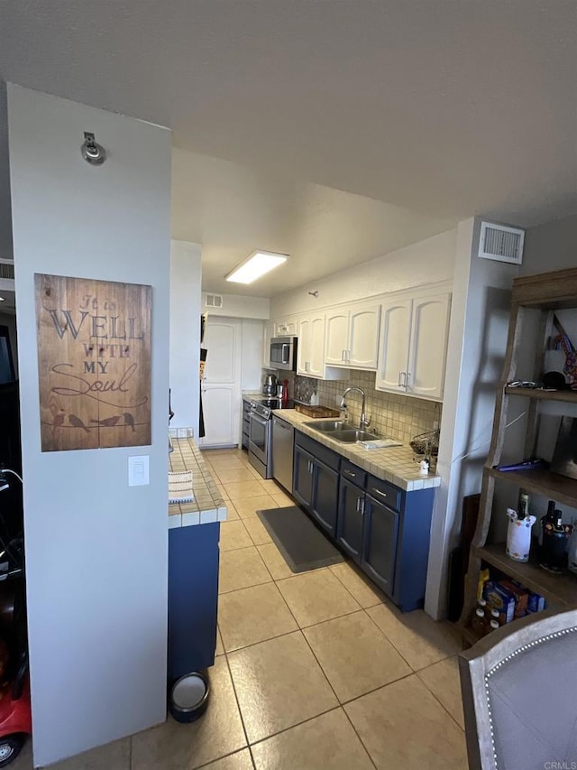 kitchen featuring light tile patterned floors, white cabinetry, stainless steel appliances, tile counters, and sink