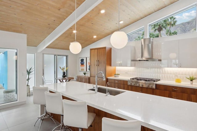 kitchen featuring white cabinetry, sink, hanging light fixtures, and wall chimney range hood