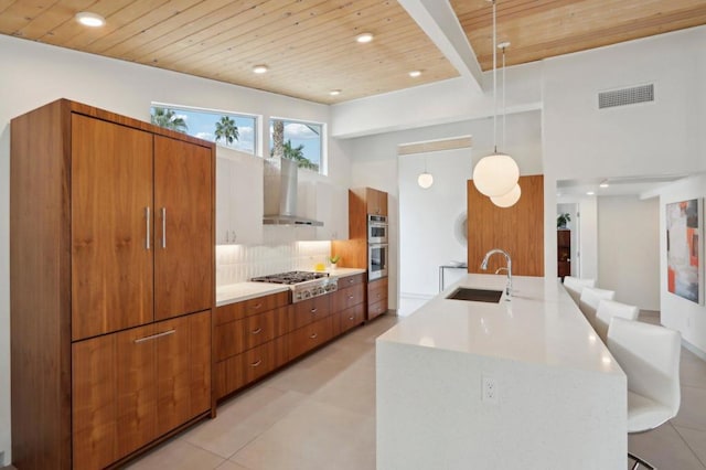 kitchen with stainless steel appliances, decorative backsplash, wall chimney range hood, pendant lighting, and sink