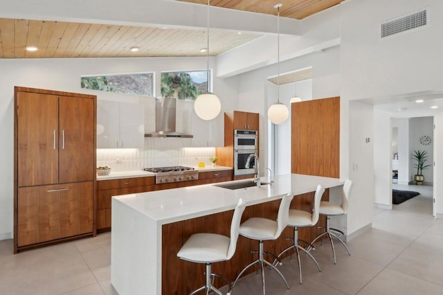 kitchen featuring white cabinets, wall chimney exhaust hood, stainless steel appliances, tasteful backsplash, and hanging light fixtures