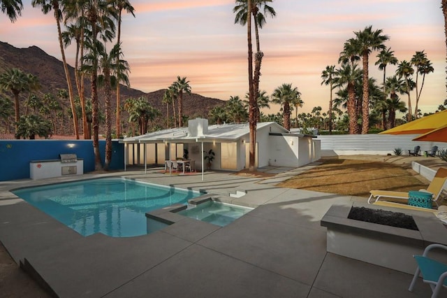 pool at dusk featuring a mountain view, a patio area, an in ground hot tub, and exterior kitchen