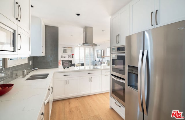 kitchen with light stone countertops, appliances with stainless steel finishes, white cabinetry, island exhaust hood, and sink