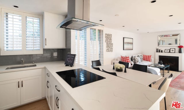 kitchen with sink, island exhaust hood, white cabinetry, light stone counters, and black electric cooktop