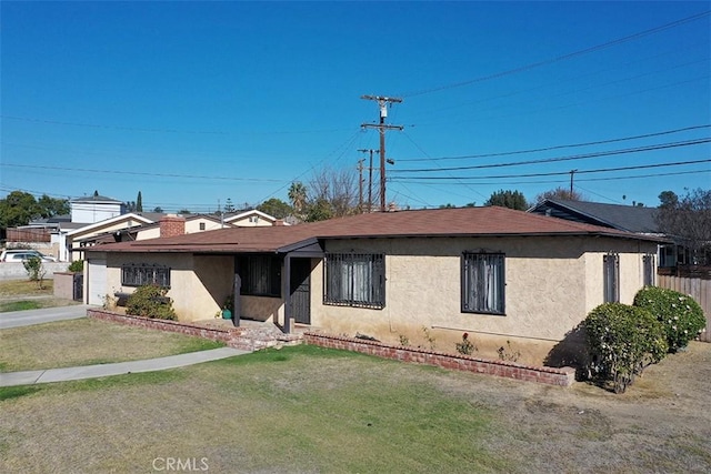 view of front of home with stucco siding, a front yard, and fence