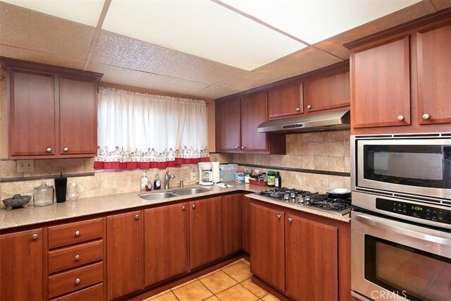 kitchen with backsplash, sink, a paneled ceiling, appliances with stainless steel finishes, and light tile patterned floors