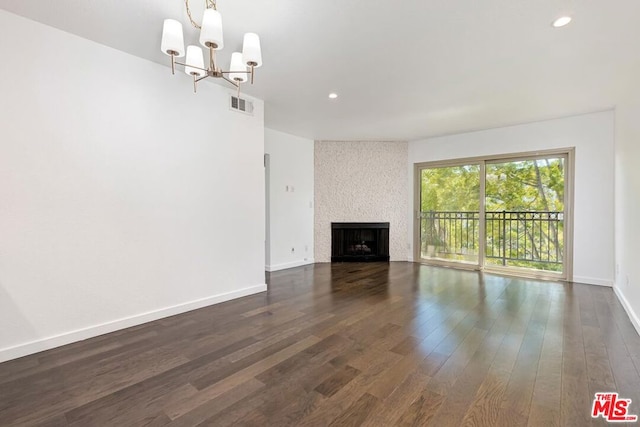 unfurnished living room with dark wood-type flooring, a fireplace, and an inviting chandelier