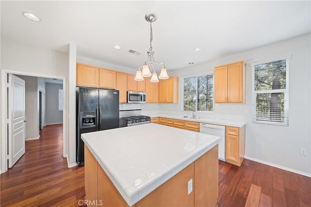 kitchen featuring decorative light fixtures, light brown cabinetry, a center island, and stainless steel appliances