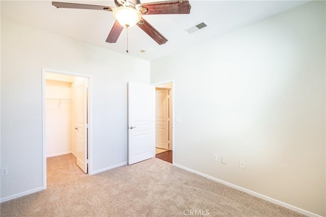 unfurnished bedroom featuring a closet, a walk in closet, light colored carpet, and ceiling fan