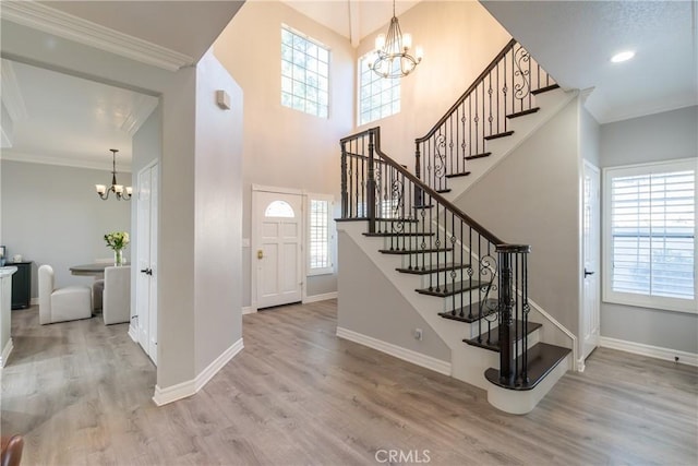 foyer with light wood-type flooring, crown molding, and an inviting chandelier