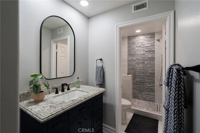 bathroom featuring toilet, vanity, and a tile shower