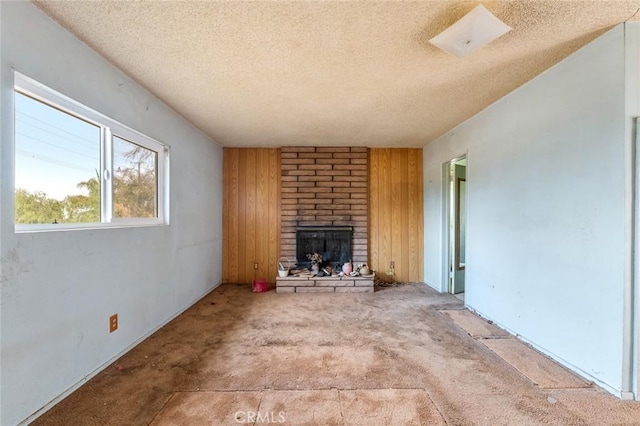 unfurnished living room featuring carpet floors, a fireplace, wooden walls, and a textured ceiling