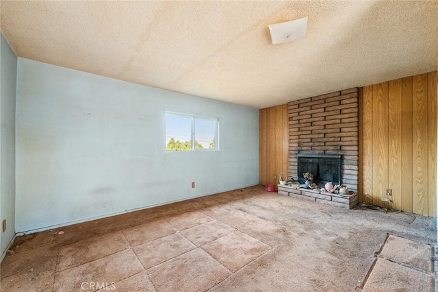 unfurnished living room with a brick fireplace, a textured ceiling, and wood walls