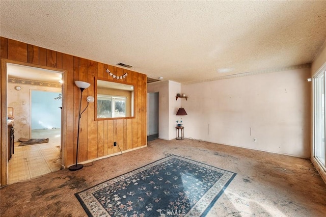 unfurnished living room featuring a textured ceiling and wood walls