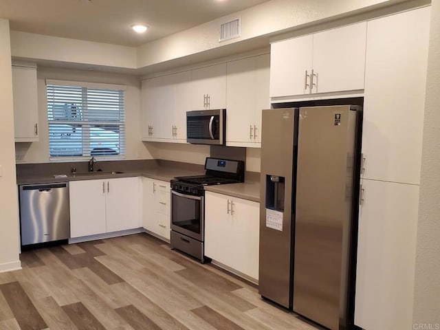 kitchen with white cabinets, appliances with stainless steel finishes, sink, and light hardwood / wood-style floors