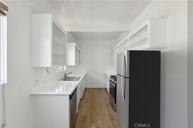 kitchen featuring white cabinets, stainless steel appliances, sink, light wood-type flooring, and beam ceiling