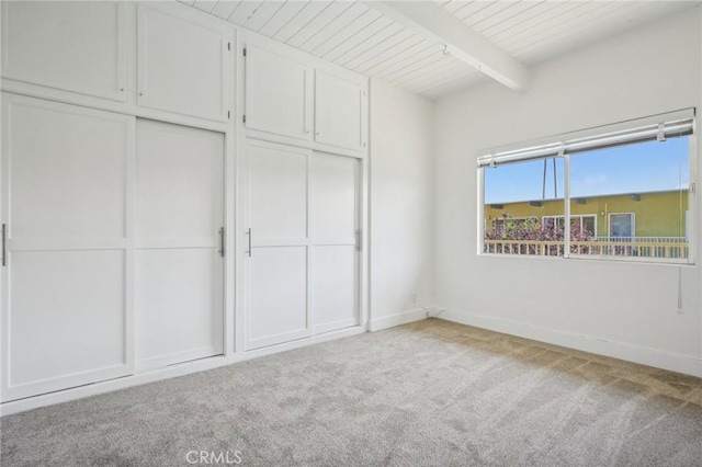 unfurnished bedroom with carpet floors, wooden ceiling, a closet, and beamed ceiling