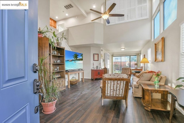 living room featuring ceiling fan, a high ceiling, dark hardwood / wood-style floors, and beam ceiling