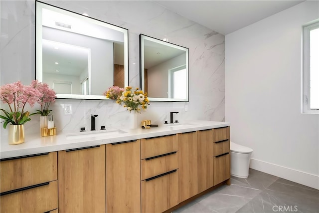 bathroom with toilet, vanity, backsplash, and a healthy amount of sunlight