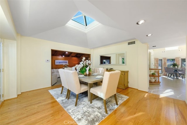 dining room featuring vaulted ceiling with skylight and light hardwood / wood-style floors