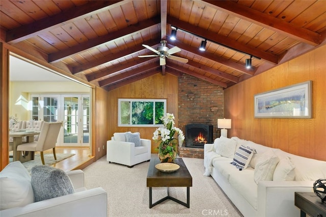 living room with wooden walls, lofted ceiling with beams, carpet flooring, wood ceiling, and a brick fireplace