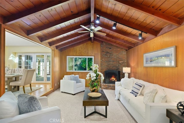 carpeted living room featuring wood ceiling, vaulted ceiling with beams, a fireplace, track lighting, and wood walls