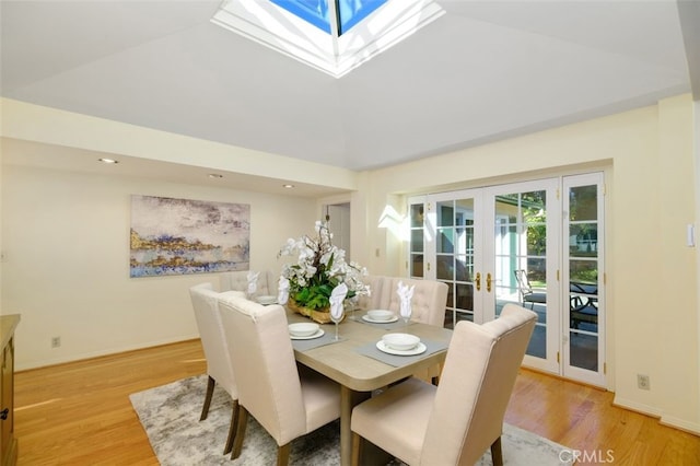 dining space with vaulted ceiling with skylight, light wood-type flooring, and french doors