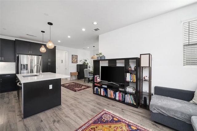 kitchen featuring decorative light fixtures, light hardwood / wood-style floors, sink, stainless steel fridge, and a kitchen island with sink