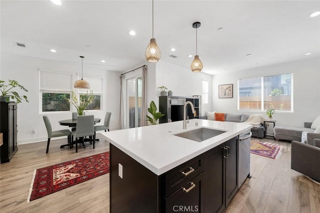 kitchen with sink, hanging light fixtures, a center island with sink, and light wood-type flooring