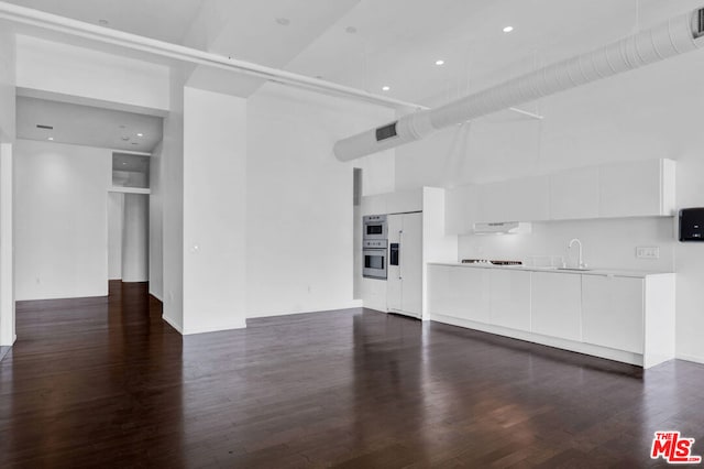 unfurnished living room featuring a high ceiling, dark hardwood / wood-style flooring, and sink