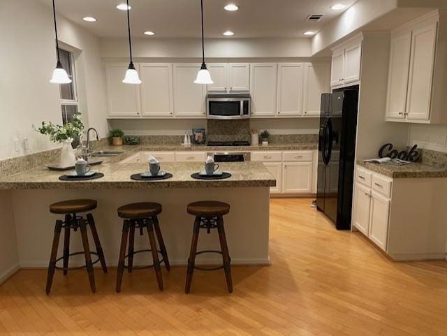 kitchen featuring black refrigerator with ice dispenser, kitchen peninsula, white cabinetry, hanging light fixtures, and a breakfast bar area