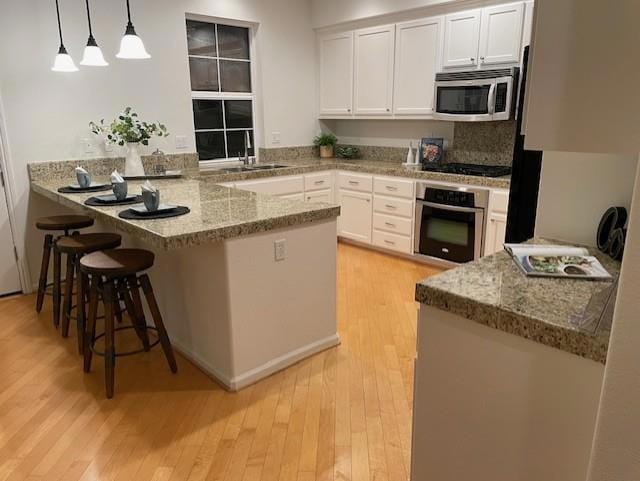 kitchen featuring pendant lighting, appliances with stainless steel finishes, white cabinetry, a kitchen breakfast bar, and kitchen peninsula