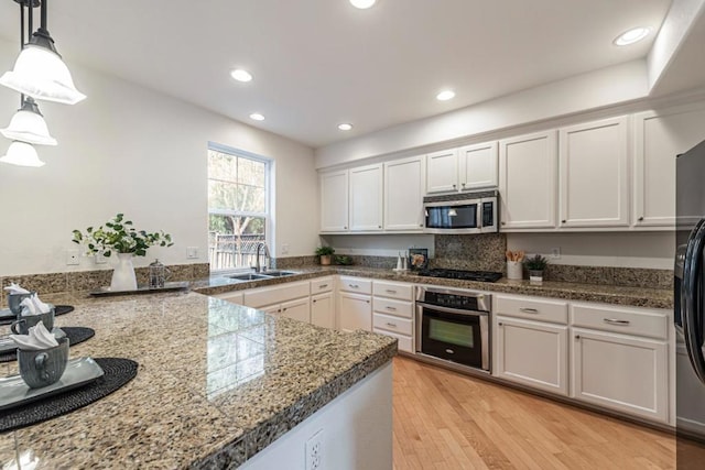 kitchen with sink, light hardwood / wood-style flooring, stainless steel appliances, white cabinets, and decorative light fixtures