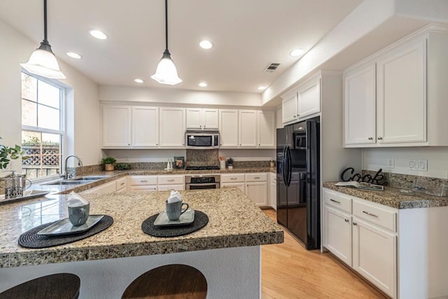 kitchen featuring sink, white cabinets, hanging light fixtures, light stone counters, and stainless steel appliances