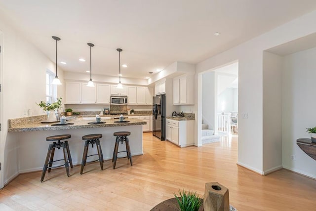 kitchen with white cabinetry, decorative light fixtures, light hardwood / wood-style flooring, black refrigerator, and kitchen peninsula