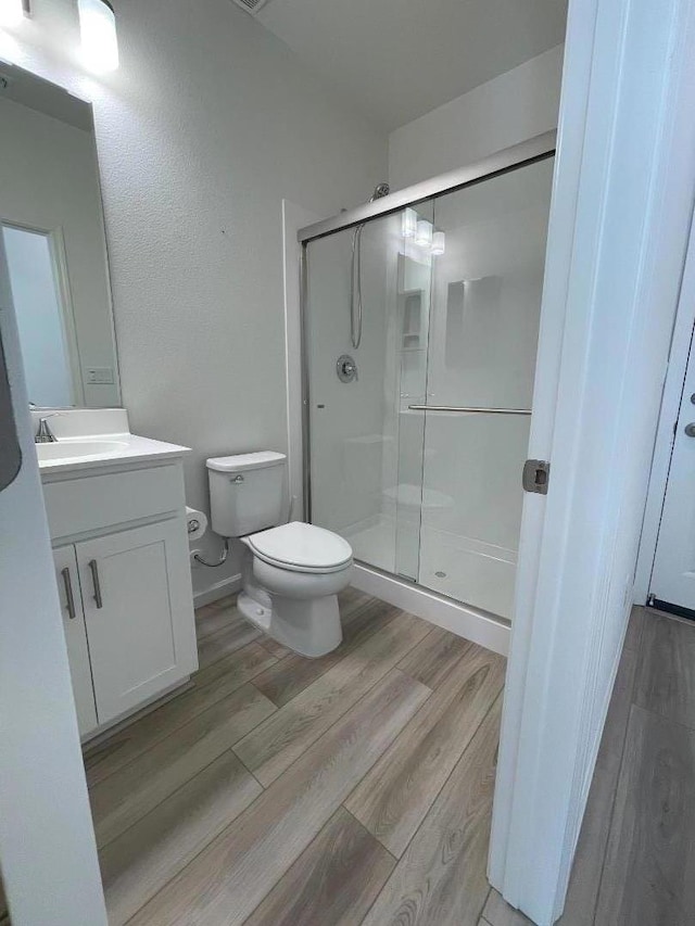 bathroom with hardwood / wood-style flooring, toilet, walk in shower, and vanity