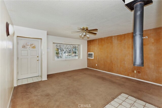 carpeted empty room featuring a textured ceiling, ceiling fan, wood walls, and a wall mounted air conditioner