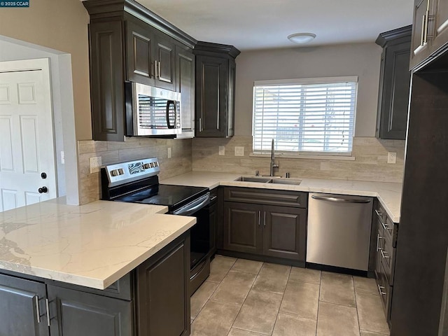 kitchen with light tile patterned flooring, appliances with stainless steel finishes, tasteful backsplash, sink, and kitchen peninsula