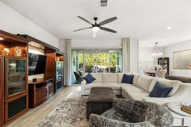 living room featuring ceiling fan with notable chandelier and light wood-type flooring