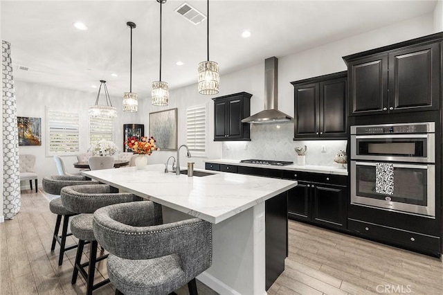 kitchen with tasteful backsplash, sink, a kitchen island with sink, a breakfast bar area, and wall chimney exhaust hood