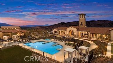 pool at dusk featuring a mountain view, a hot tub, and a patio