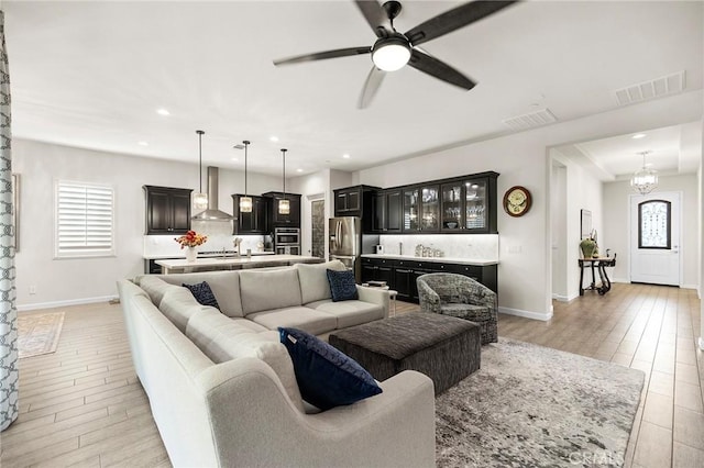 living room with ceiling fan with notable chandelier and light hardwood / wood-style floors