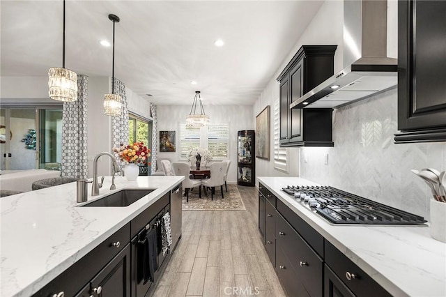 kitchen featuring sink, pendant lighting, wall chimney exhaust hood, and a notable chandelier