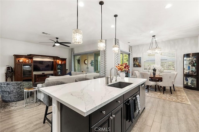 kitchen with ceiling fan, sink, a center island with sink, and pendant lighting