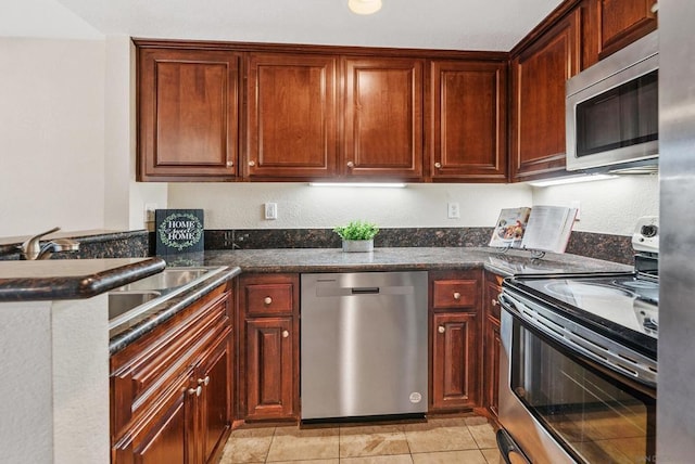 kitchen featuring light tile patterned flooring, stainless steel appliances, and dark stone counters