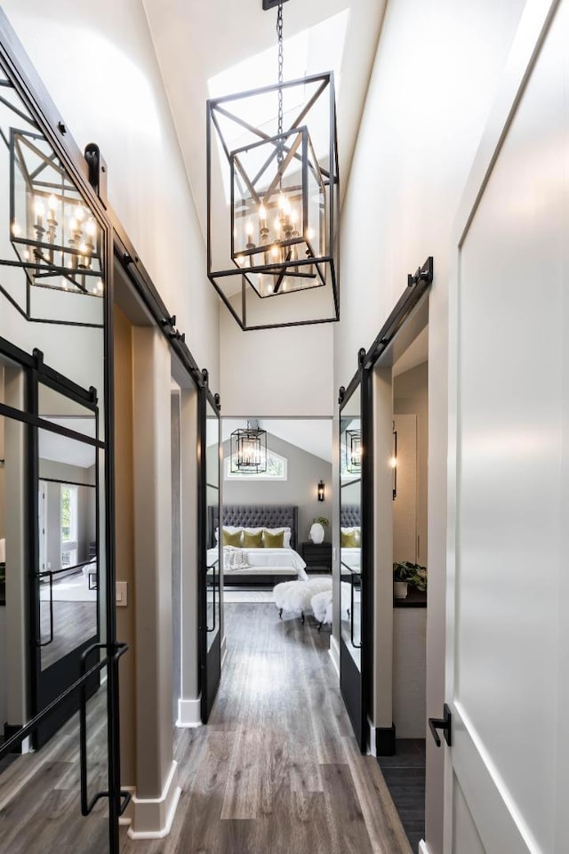 hall featuring dark hardwood / wood-style floors, a barn door, a high ceiling, and a notable chandelier