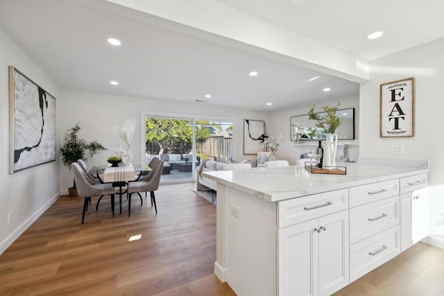 kitchen with hardwood / wood-style flooring, kitchen peninsula, white cabinets, and light stone counters