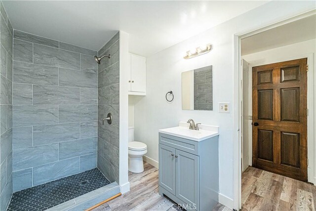 bathroom featuring hardwood / wood-style floors, toilet, vanity, and a tile shower