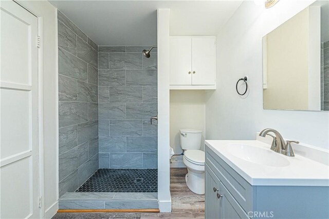 bathroom with toilet, hardwood / wood-style flooring, tiled shower, and vanity